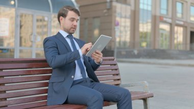 Young Businessman using Tablet while Sitting Outdoor on Bench