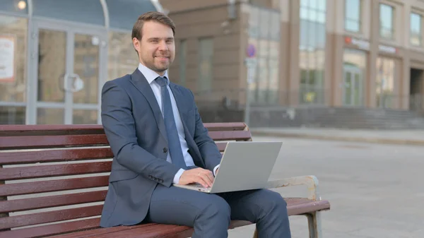 Young Businessman Shaking Head in Approval While using Laptop Sitting Outdoor on Bench
