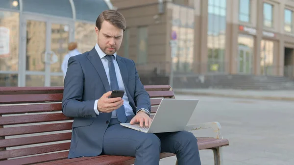 Young Businessman Using Smartphone Laptop While Sitting Outdoor Bench — Φωτογραφία Αρχείου