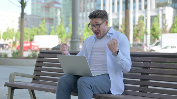 Middle Aged Man Celebrating Success on Laptop while Sitting Outdoor on Bench