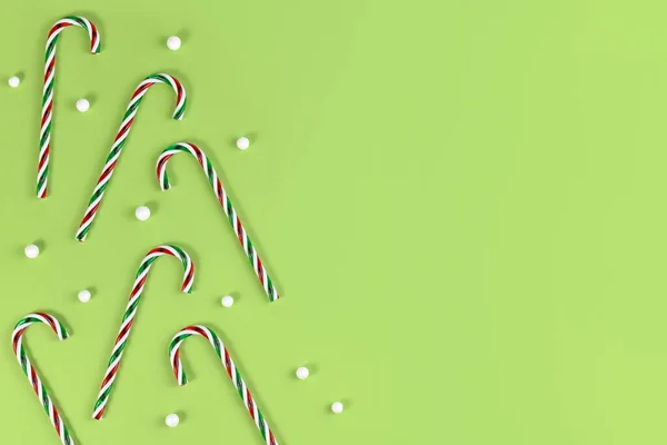 コピースペース付きの緑の背景の上に雪玉付きのストライプのキャンディー杖クリスマスお菓子 — ストック写真
