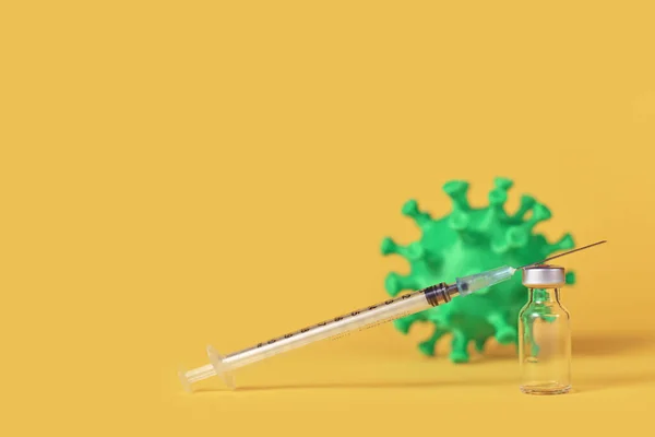 Corona vaccine vial with syringe and virus model in background on yellow background with copy space