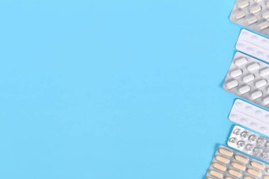 Kabarcık paketlerindeki farklı kapsüller ve haplar mavi arkaplanın sağ tarafında fotokopi alanı ile