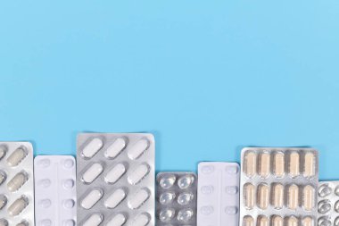 Mavi arkaplanın altında çeşitli haplar ve kapsüller içeren kabarcık paketleri.