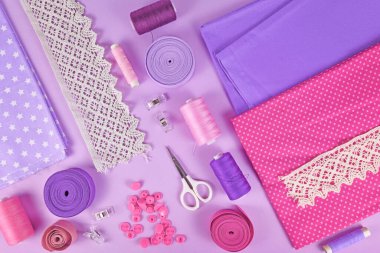 Düz dikiş, kumaş, makas, makaralar ve menekşe arkaplanda kurdele gibi çeşitli araçlarla.