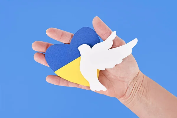 Hand holding dove of peace and heart with Ukraine flag colors blue and yellow