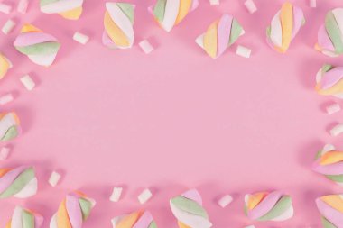 Pastel renkli şekerlemeler pembe arkaplan etrafında çerçeve oluşturuyor