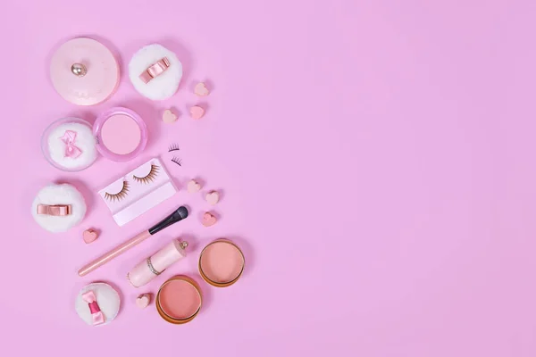 Pink makeup beauty products like brushes, powder or lipstick on side of pastel pink background with empty copy space