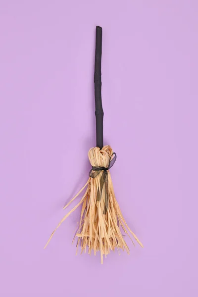 Witch broom with black twig and straw bristles on violet background