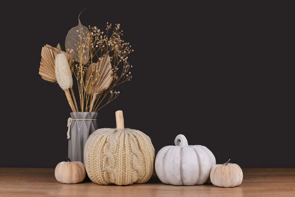 Fall decoration with boho style knitted beige pumpkin and gray stone pumpkin on dark backgroun