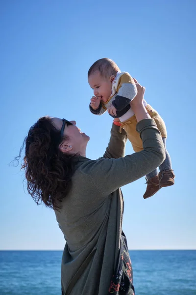 Kvinna som håller sitt leende barn i famnen på en stranddag — Stockfoto