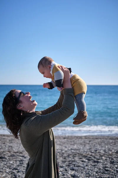 Kvinna som håller sitt leende barn i famnen på en stranddag — Stockfoto