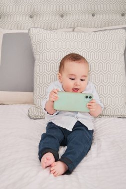 Yatakta oturan akıllı telefonu kullanan bir bebek