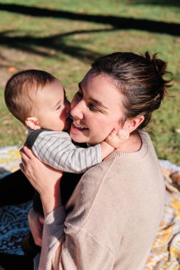 Güneşli bir günde bebeğiyle parkta oynayan genç bir kadın.