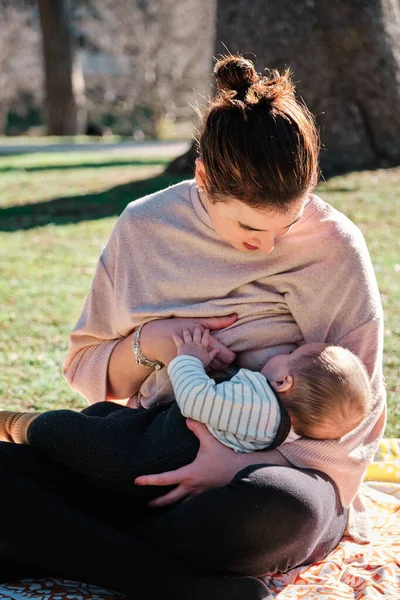 Ung kvinna ammar sin son utomhus i en allmän park — Stockfoto