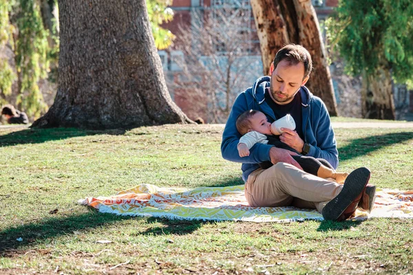 Ung man flaska mata sin son utomhus i en allmän park — Stockfoto