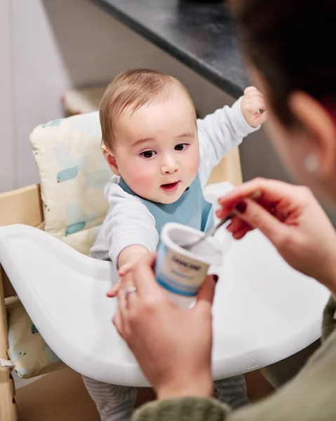 Mor ger en yoghurt till sin son som sitter i barnstolen — Stockfoto