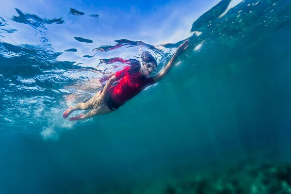 View from bellow of a young girl swimming at the sea with a mask an a snorkel