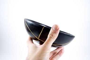 İzole edilmiş siyah Japon kintsugi kasesi, altın çatlaklarıyla restore edilmiş antika çömlek. Geleneksel altın düzeltme yöntemi.