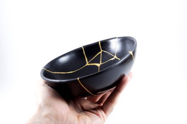 İzole edilmiş siyah Japon kintsugi kasesi, altın çatlaklarıyla restore edilmiş antika çömlek. Geleneksel altın düzeltme yöntemi.