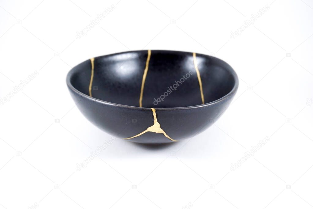 Gold cracks Kintsugi, broken black repaired bowl, Japanese technique.