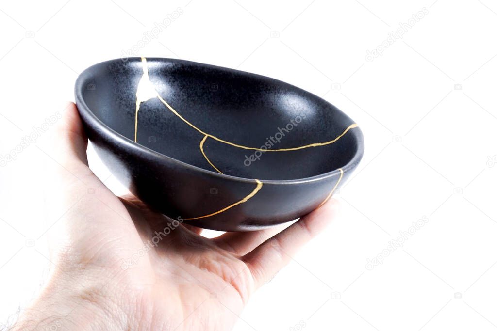 Gold cracks Kintsugi, broken black repaired bowl, Japanese technique.