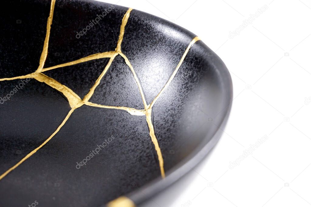 Isolated black Japanese kintsugi bowl, antique pottery restored with gold cracks. Traditional gold fixing method.