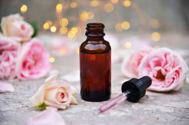 Gül çiçekleri ve bokeh arka planında bir şişe gül yağı.