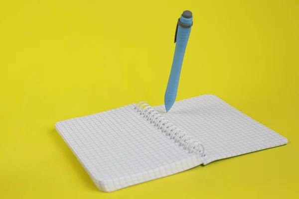 ノートパッドを開き 黄色の背景にペンを持ち上げます 執筆コンセプト — ストック写真