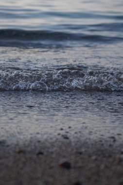 Dalgaların ve kabarcıkların yakın çekimi deniz kenarında, berrak mavi su