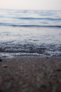 Dalgaların ve kabarcıkların yakın çekimi deniz kenarında, berrak mavi su