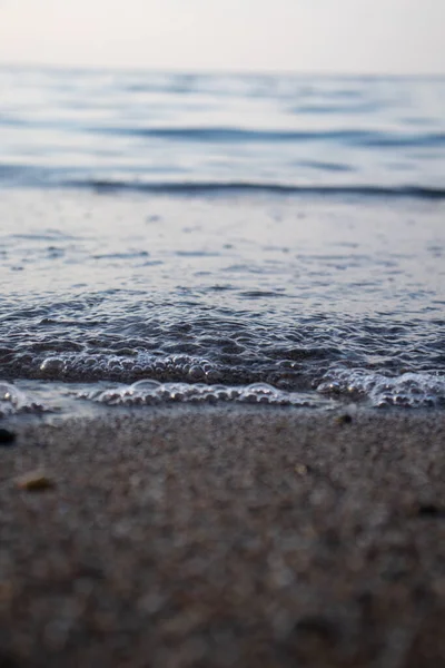 Dalgaların ve kabarcıkların yakın çekimi deniz kenarında, berrak mavi su