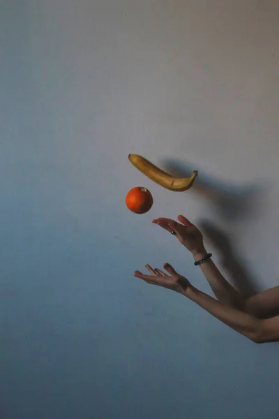 Female hands throwing a orange and a banana in the air, blue background