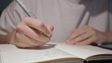Genç kız öğrenci, beyaz kağıt sayfalarla kalemle yavaş çekimde not defteri yazıyor.