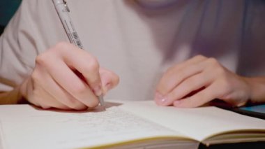 Genç öğrenci ödevlerini beyaz kâğıt defterle yapıyor. Ağır çekimde.