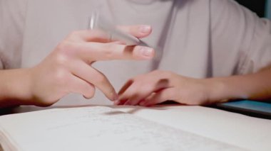 Kalemle oynayan tembel, genç bir öğrenci hassas ellerin arasında.