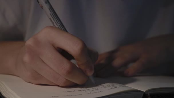 Jonge vrouw handen houden pen schrijven dagboek op wit papier pagina 's in donkere kamer — Stockvideo