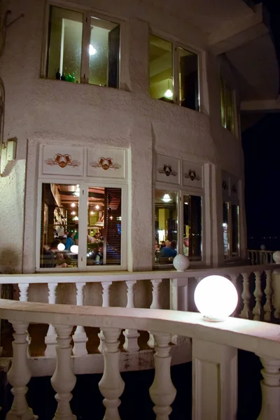 Akşam geç saatlerde panoramik pencerelerde yemek yiyen tanınmayan insanlarla dolu şık bir restoran balkon terası..