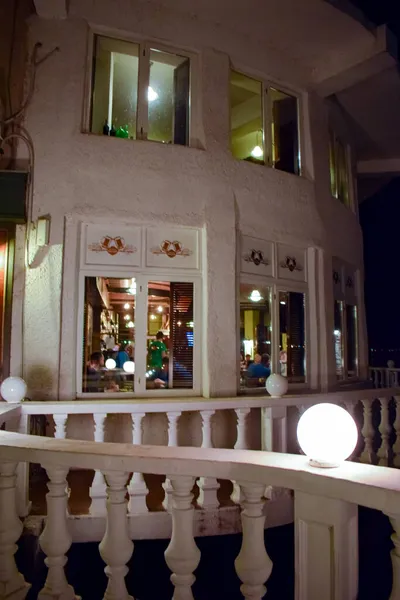 Akşam geç saatlerde panoramik pencerelerde yemek yiyen tanınmayan insanlarla dolu şık bir restoran balkon terası..