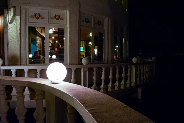 Akşam geç saatlerde panoramik pencerelerde yemek yiyen tanınmayan insanlarla dolu şık bir restoran balkon terası..