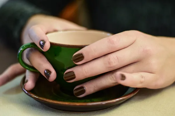 Młoda kobieta ręce z ciemnym lakierem paznokci gospodarstwa piękny ciemnozielony filiżanka kawy na talerzu z gorącą zieloną herbatą — Zdjęcie stockowe