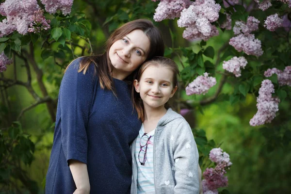妈妈和女儿在一朵盛开的紫丁香树下摆姿势 — 图库照片