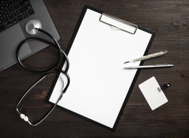 Doktorun tıbbi malzemeleri. Boş tıbbi pano, steteskop, rozet, termometre, tahta arka planda kalem ve dizüstü bilgisayar..