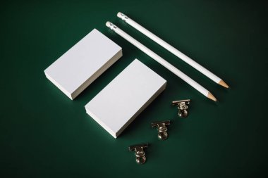 Yeşil arka planda boş kartvizitler, kalemler ve ataçlar. Boş kırtasiye seti.