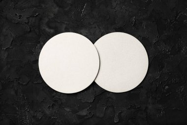 Siyah taştan arka planda iki beyaz bira altlığı. Tepkili tasarım modeli. Düz yatıyordu.