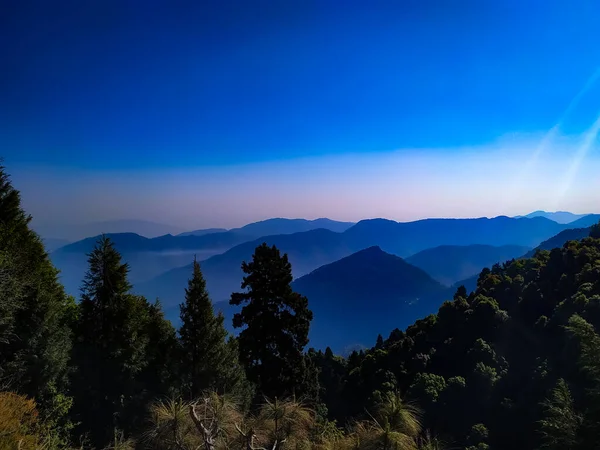 Ağaçlarla kaplı dağların üzerinde dramatik bir gün batımı