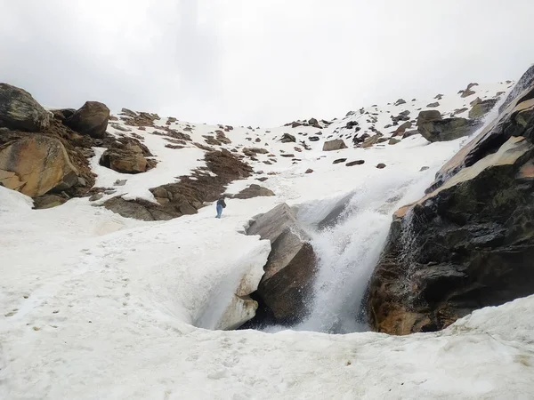 Karlı dağın tepesindeki şelale. Kaynağın suyu donmuş kar altında taş gibi kalır. Karlı bir dağın tepesindeki taşlar.