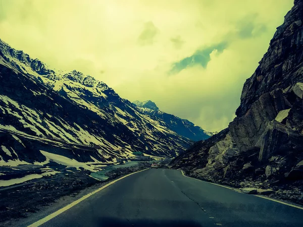 Dağlardaki asfalt yolun manzarası yol kenarındaki kar ve kayalarla kaplı gökyüzü ve bulutların arka planında