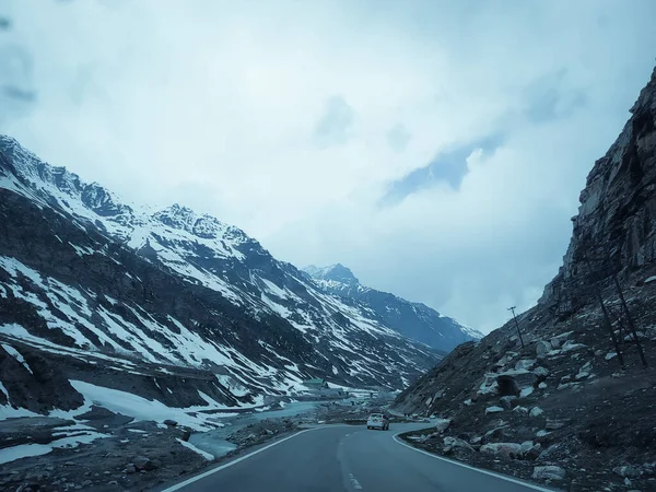 Dağlardaki asfalt yolun manzarası yol kenarındaki kar ve kayalarla kaplı gökyüzü ve bulutların arka planında