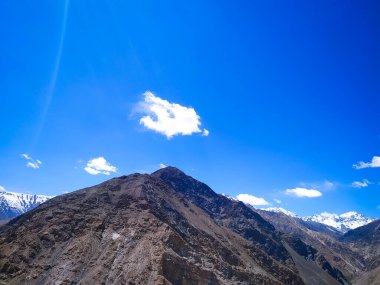 Mavi gökyüzü ve bulutlarıyla güzel bir dağ manzarası.